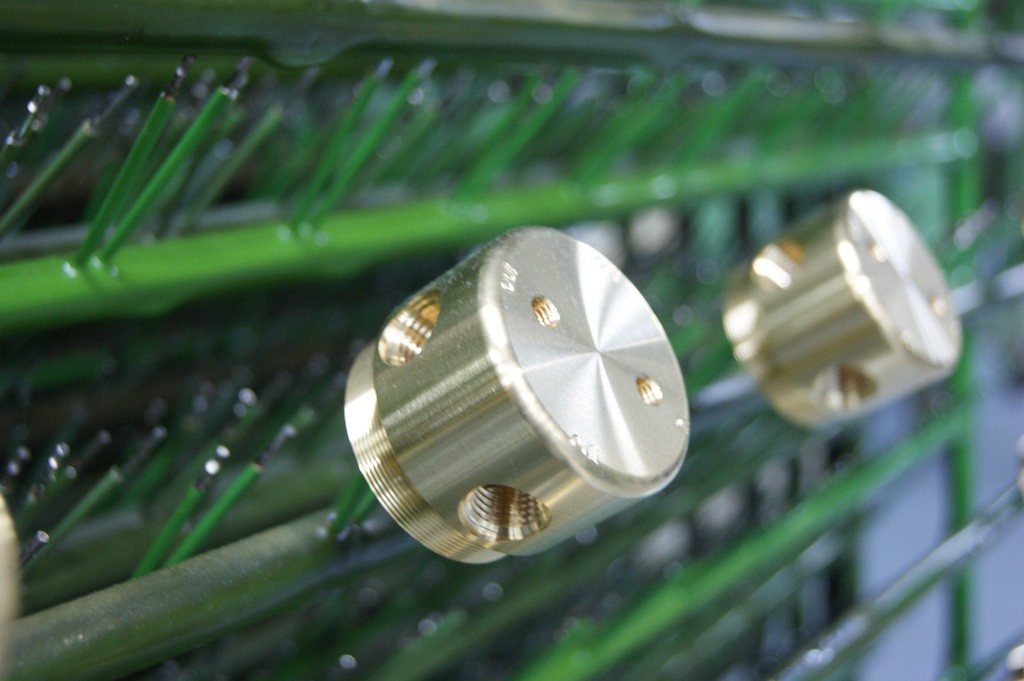 Goldfarbene Messing-Drehteile mit Gewindebohrungen hängen an grün beschichteten Warenträgern