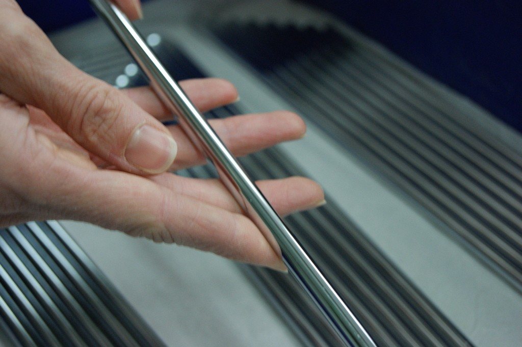 Hand hält eine spiegelnd glänzende Metallleiste über geriffelten Profilteilen zur Sichtkontrolle